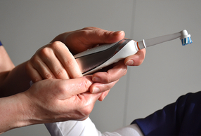 mani adulte aiutano un bambino ad impugnare uno spazzolino elettrico