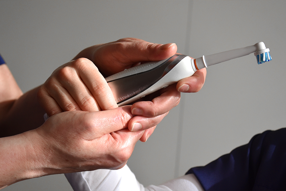 mani adulte aiutano un bambino ad impugnare uno spazzolino elettrico