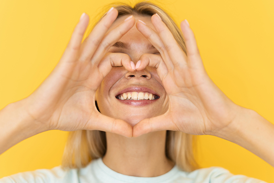 ragazza che fa simbolo del cuore con le mani davanti ad un sorriso